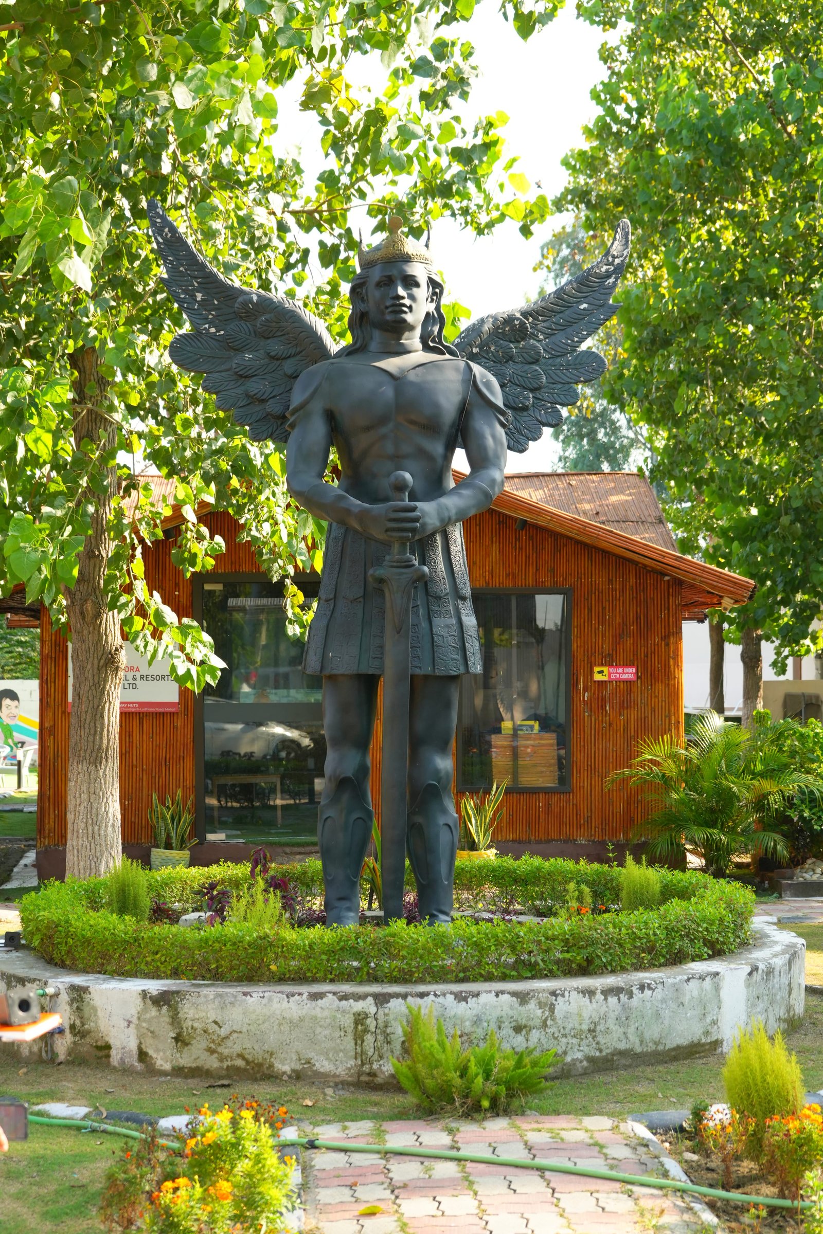 The winged figure in its planted bed, huts behind